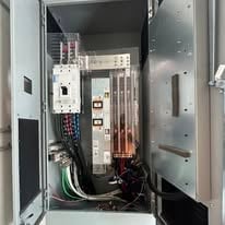 Open electrical panel with circuit breakers, wiring, and hardware mounted inside the cabinet