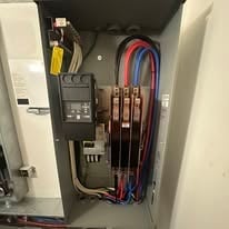 Open electrical panel showing circuit breakers, wiring, and components inside a wall cabinet